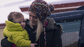 Mom holding a baby getting in her car on a snowy road